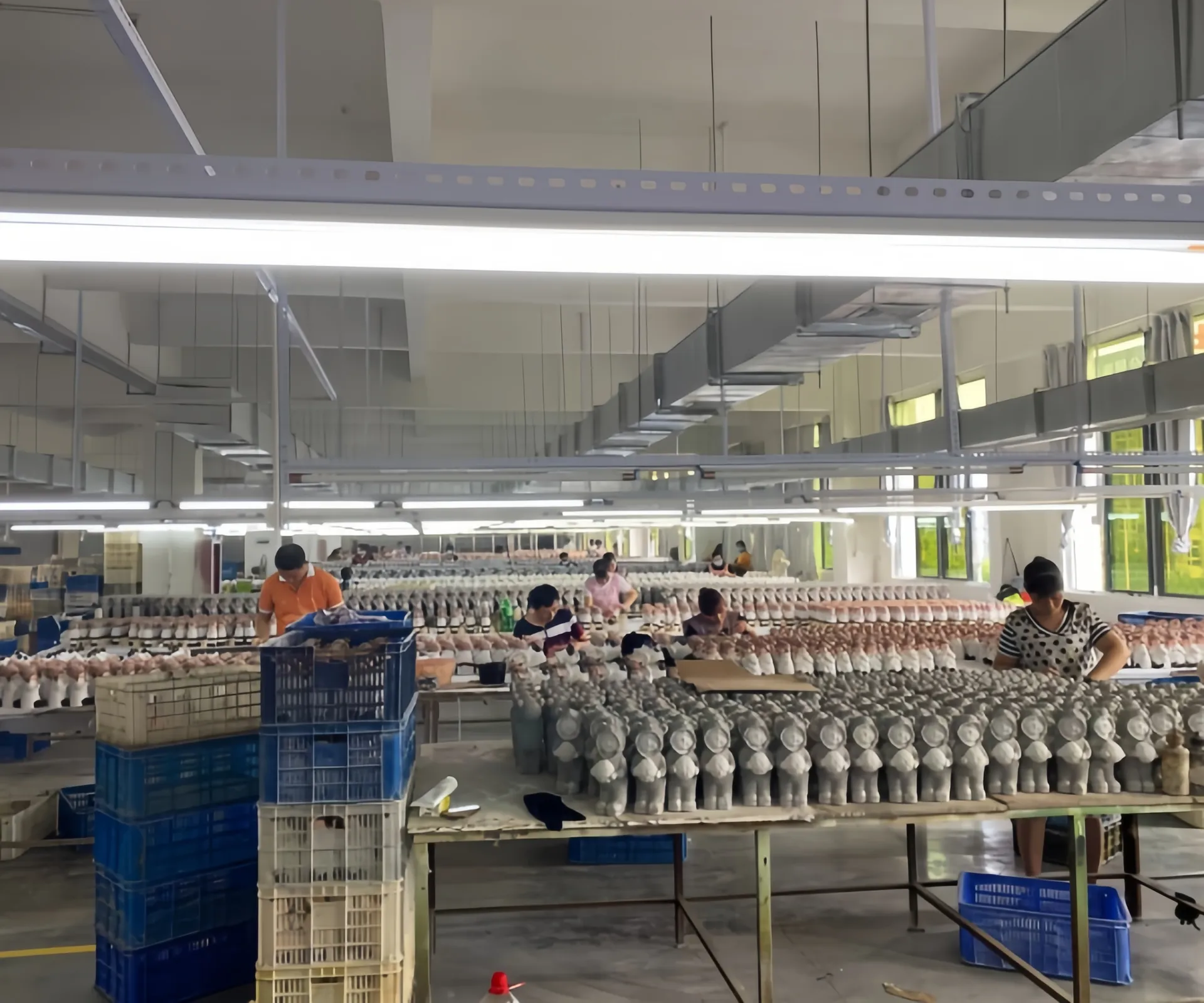 Arbeiter in einer Fabrikhalle, die Reihen von Figuren auf Tischen bemalen und zusammensetzen.