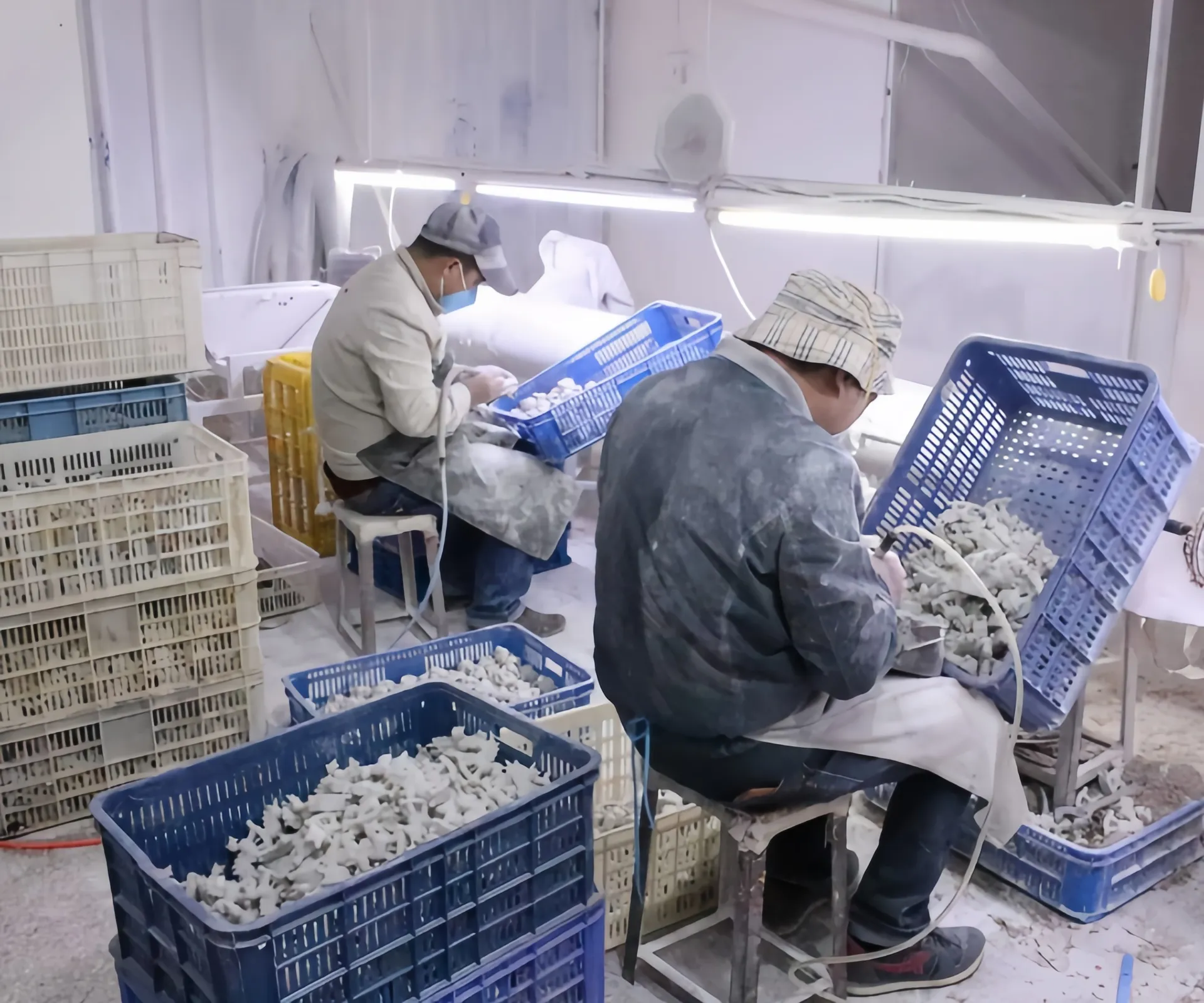 Zwei Arbeiter sortieren kleine weiße Gegenstände in Plastikkisten in einer Industrieumgebung.