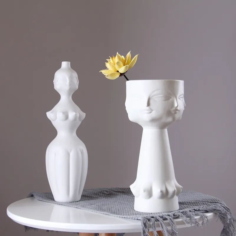 White sculptural vases with human features on a table, one with a yellow flower.