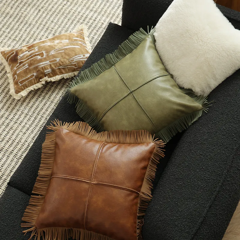 Une collection de coussins décoratifs sur un canapé, comprenant du cuir marron, du cuir vert, de la fausse fourrure blanche et des motifs marron.