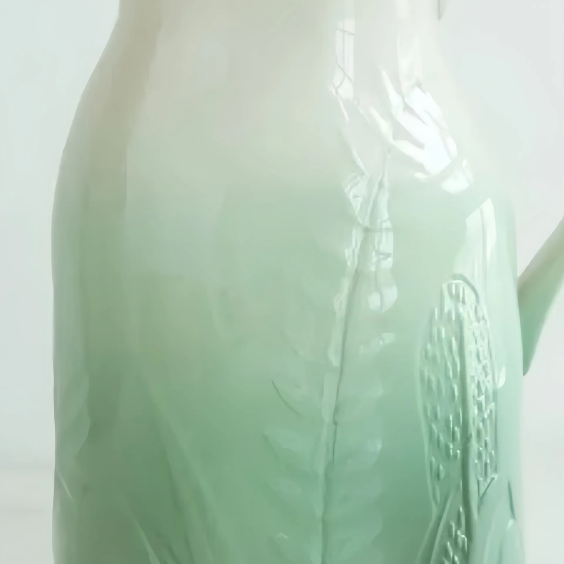Close-up of a celadon glazed vase with embossed leaf and lotus patterns.