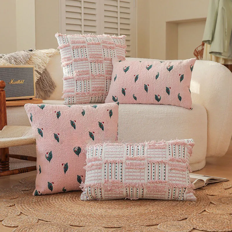 Une pièce confortable avec des coussins roses et à motifs sur un canapé blanc moelleux, un tapis tissé et un petit haut-parleur.
