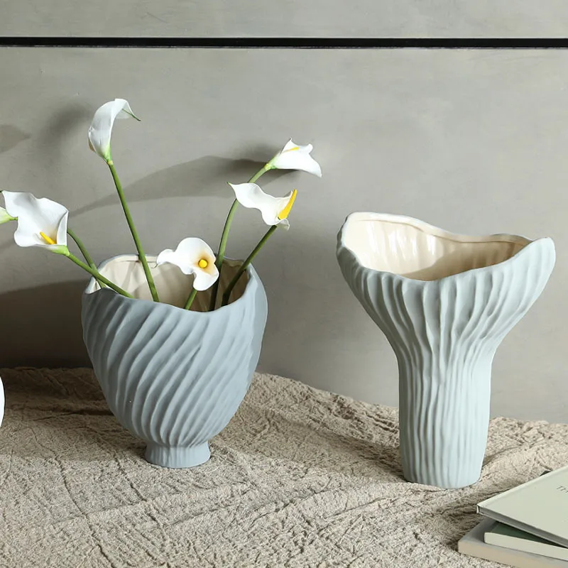 Two decorative ceramic vases on a textured surface, one filled with white flowers.