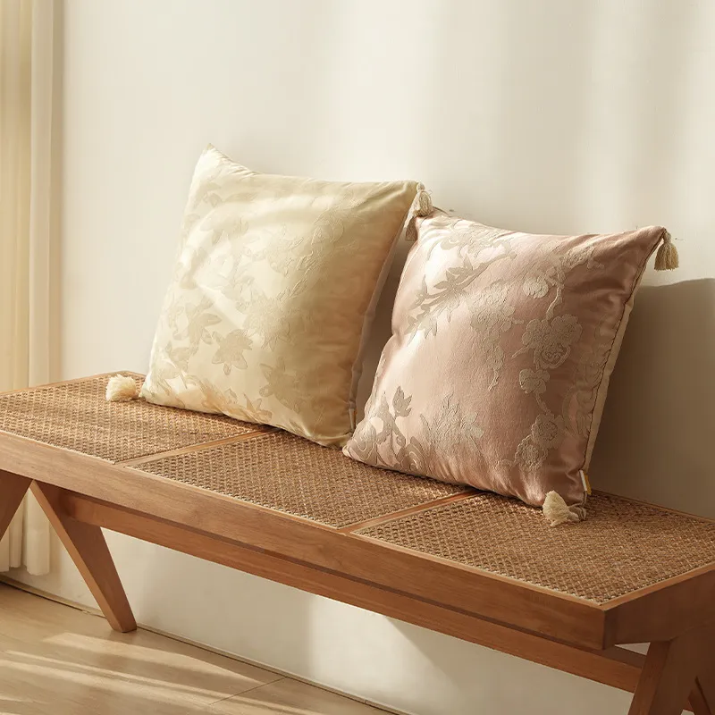 Deux coussins décoratifs, l'un crème et l'autre rose pâle, placés sur un banc en bois avec assise tissée.