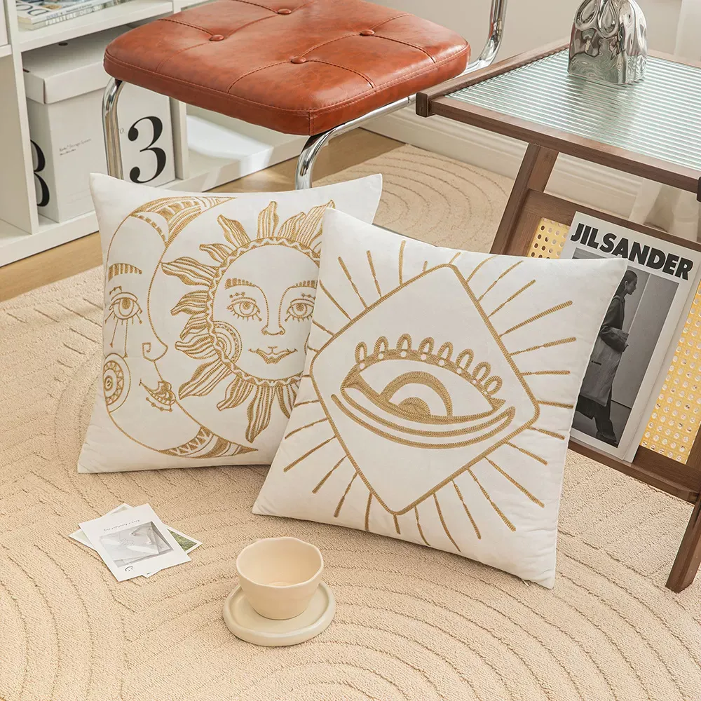 Deux coussins décoratifs avec des motifs de soleil et d'yeux, placés sur un tapis texturé à côté d'une tasse, d'une soucoupe et d'une petite table.