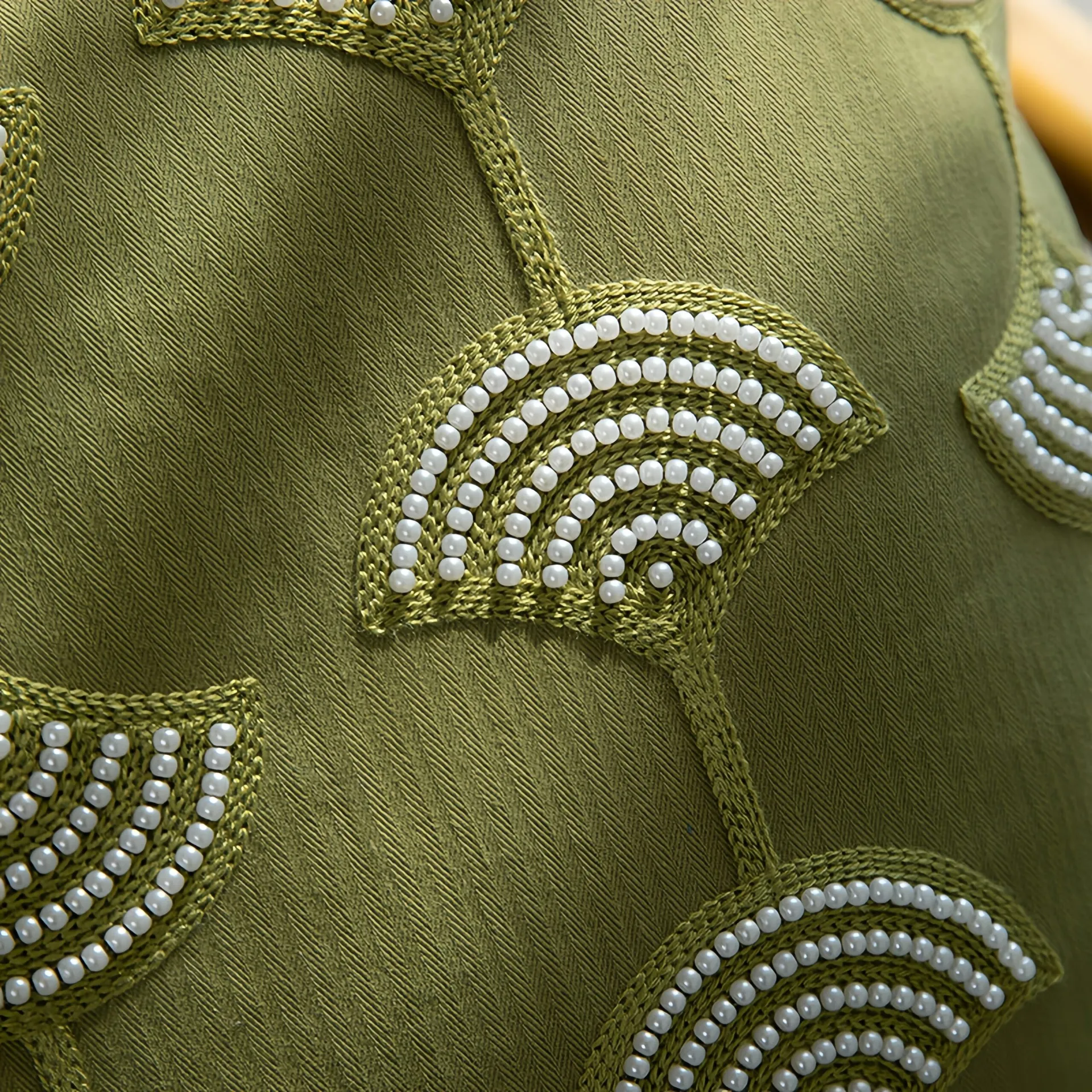 Close-up of a decorative pillow with an olive green fabric covered in pearl beaded semicircles.