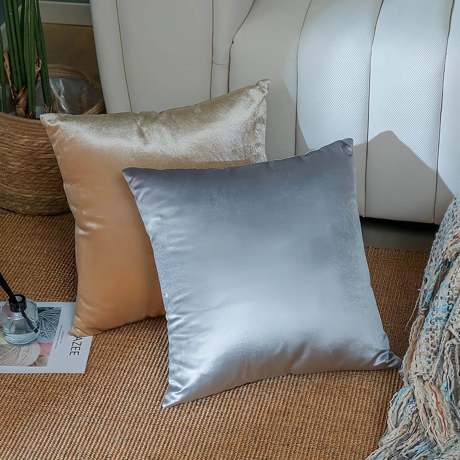 Deux coussins décoratifs brillants, l'un argenté et l'autre doré, placés sur un tapis tissé à côté d'un canapé.