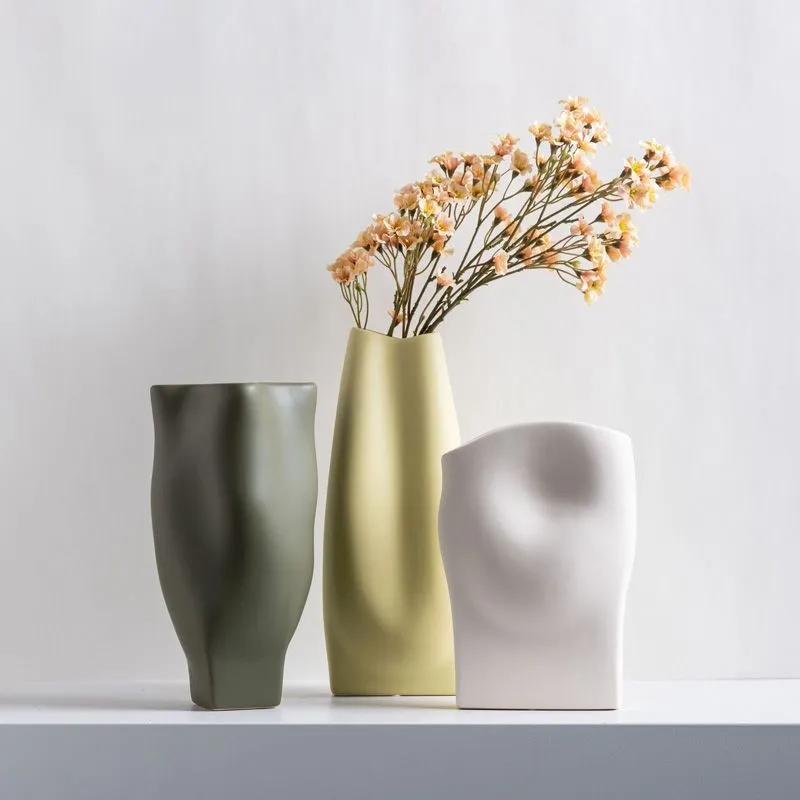 Three modern vases with flowers, one green, one beige with flowers, and one white, on a white surface.