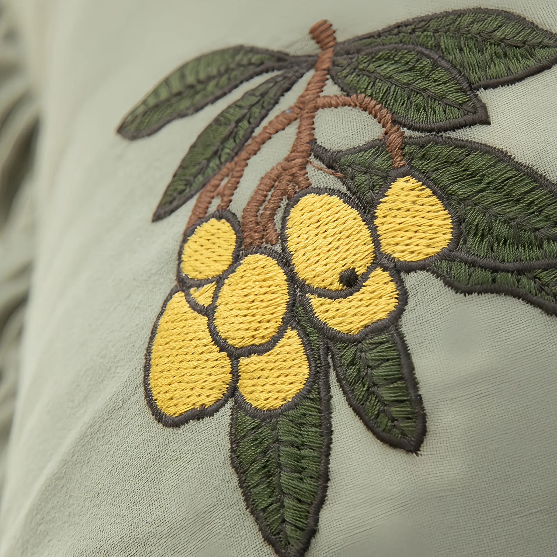 Close-up of embroidered yellow fruit and green leaves on fabric.