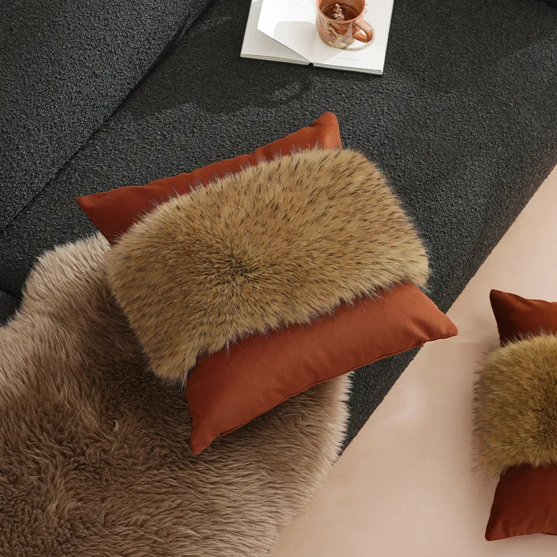 Un canapé noir avec deux oreillers décoratifs en fausse fourrure et une tasse en céramique sur l'accoudoir.