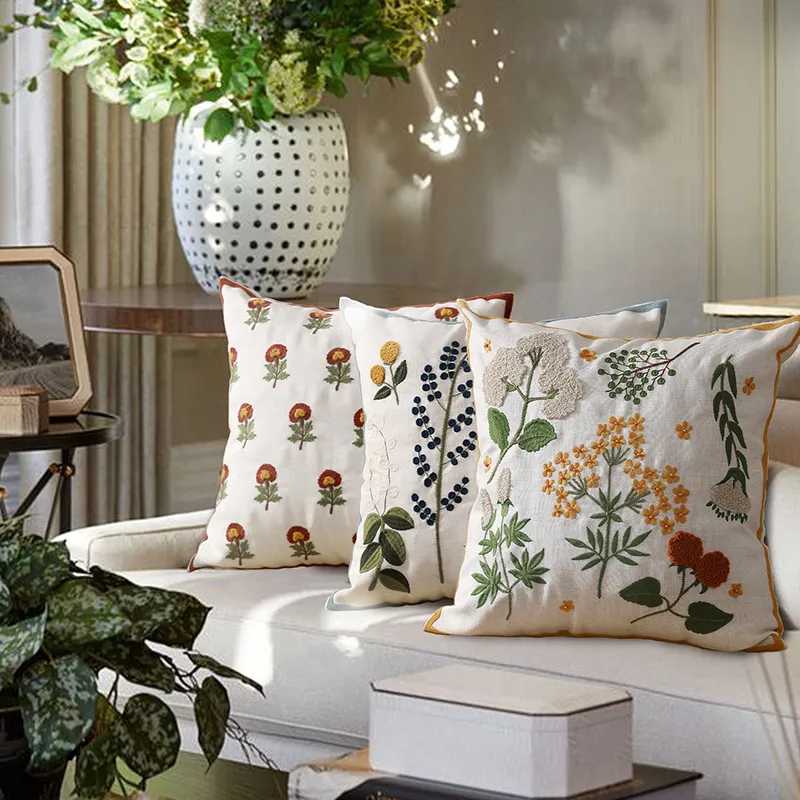 Un salon confortable avec trois coussins décoratifs à motifs floraux sur un canapé, avec un vase à pois et des fleurs en arrière-plan.