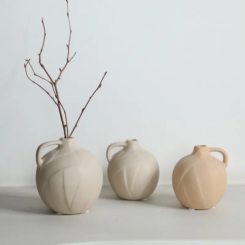 Three ceramic vases with handles, one containing twigs, placed on a neutral background.
