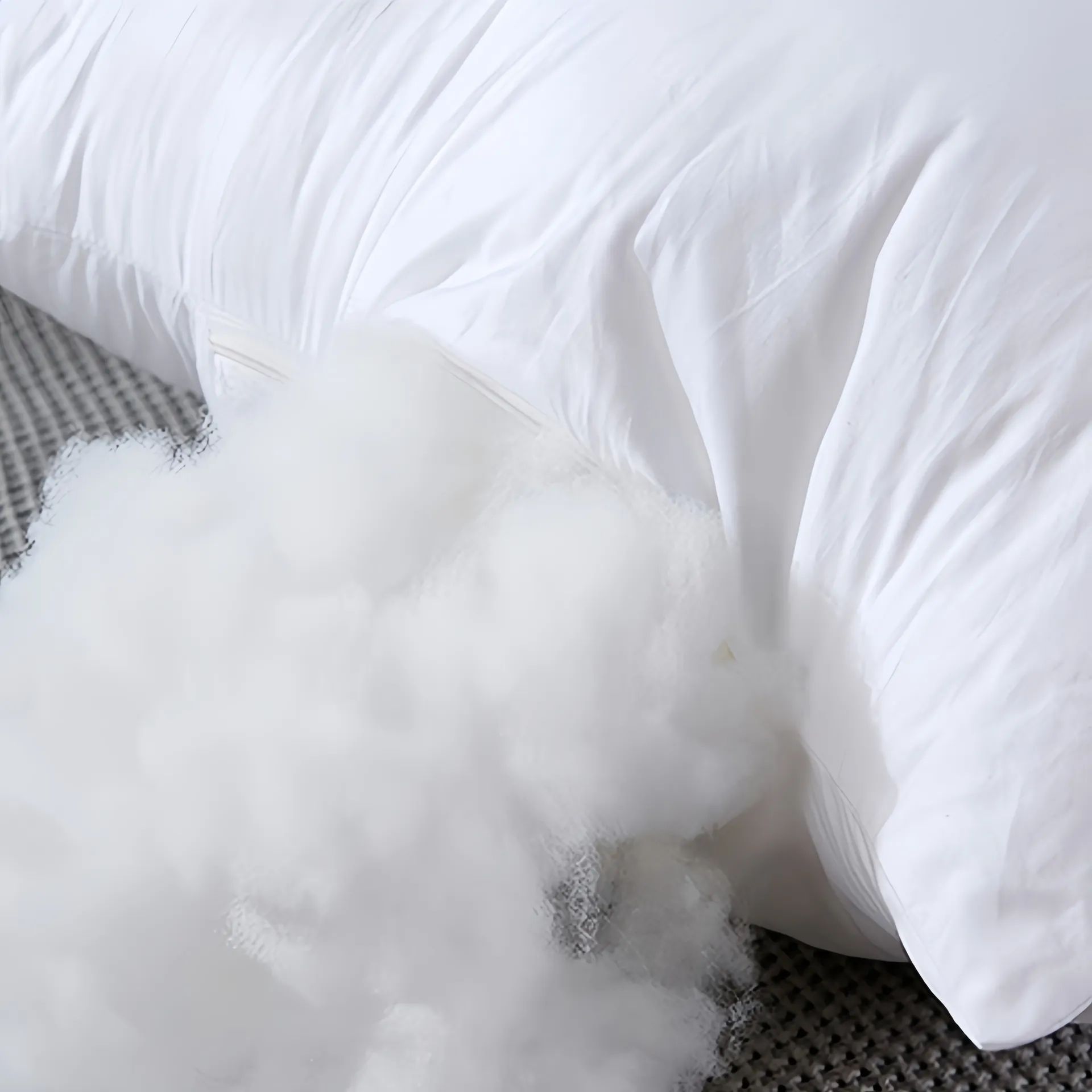 A white pillow with fiber filling spilling out onto a textured surface.