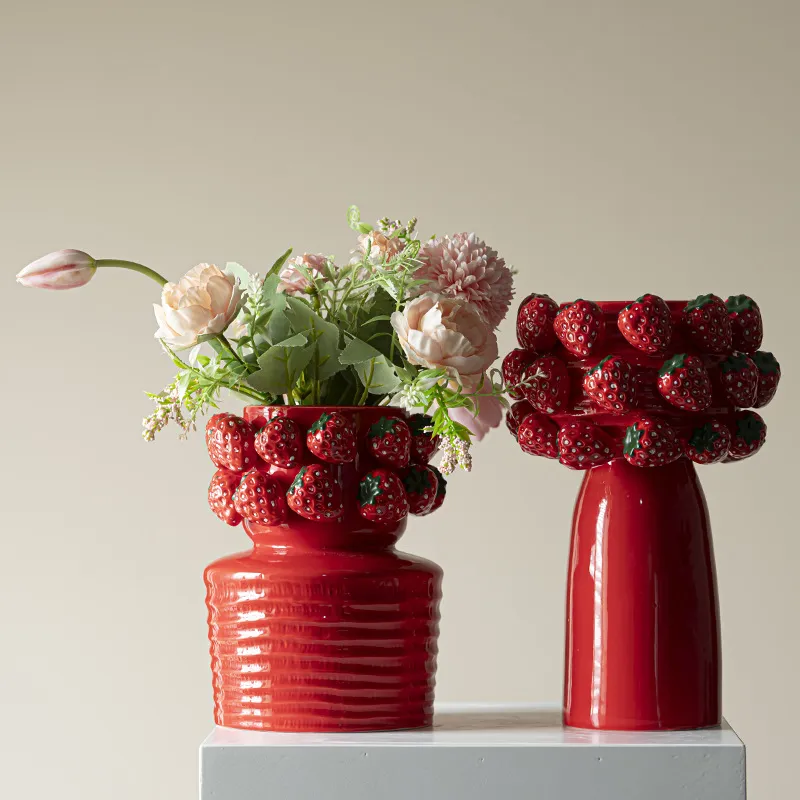 Two red ceramic vases adorned with strawberries, one holding flowers.