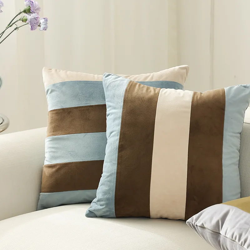Deux housses de coussin rayées aux couleurs bleu clair, marron et beige sur un canapé blanc.
