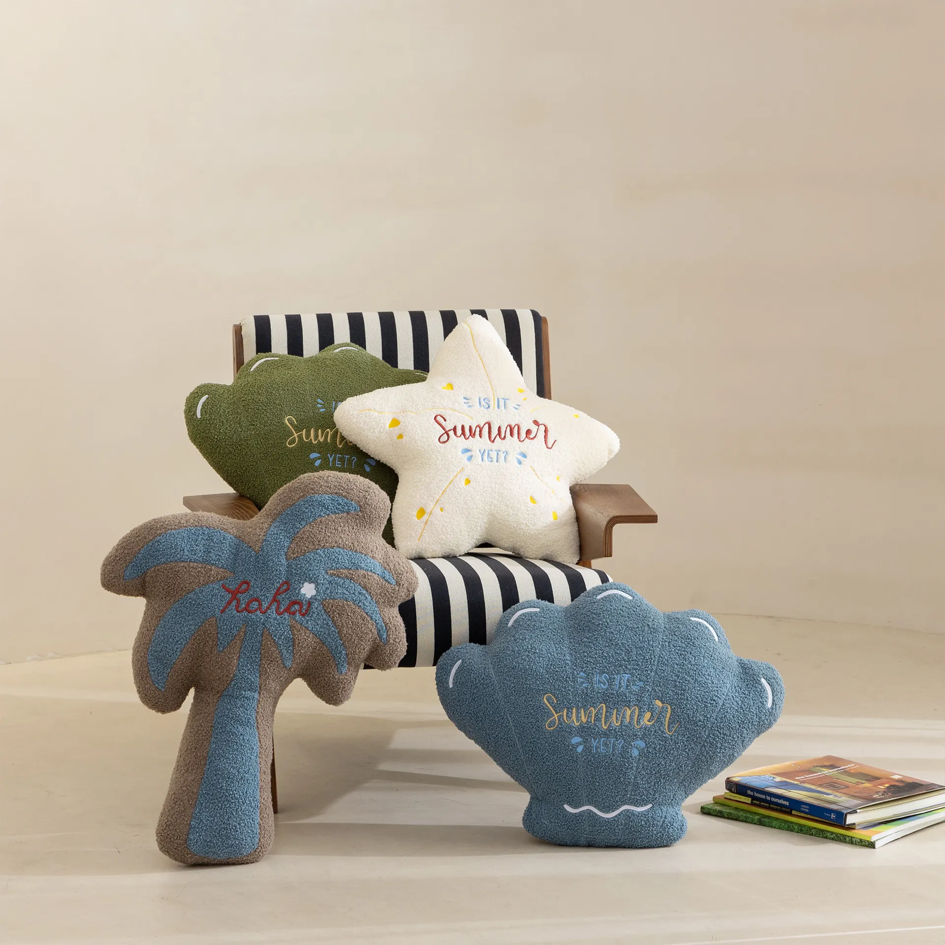 Un ensemble de coussins aux formes variées sur le thème de l'été, comprenant une étoile, un palmier et un coquillage, placés sur une chaise rayée avec des livres à proximité.