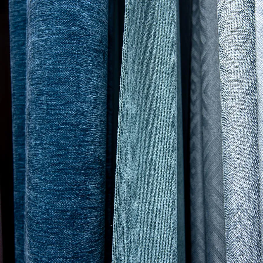 Close-up of several rolls of fabric in various shades of blue and grey, displaying different textures.