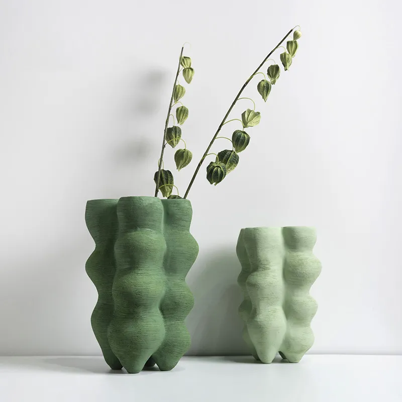 Two green vases with wavy textures, one with leafy branches, against a plain background.