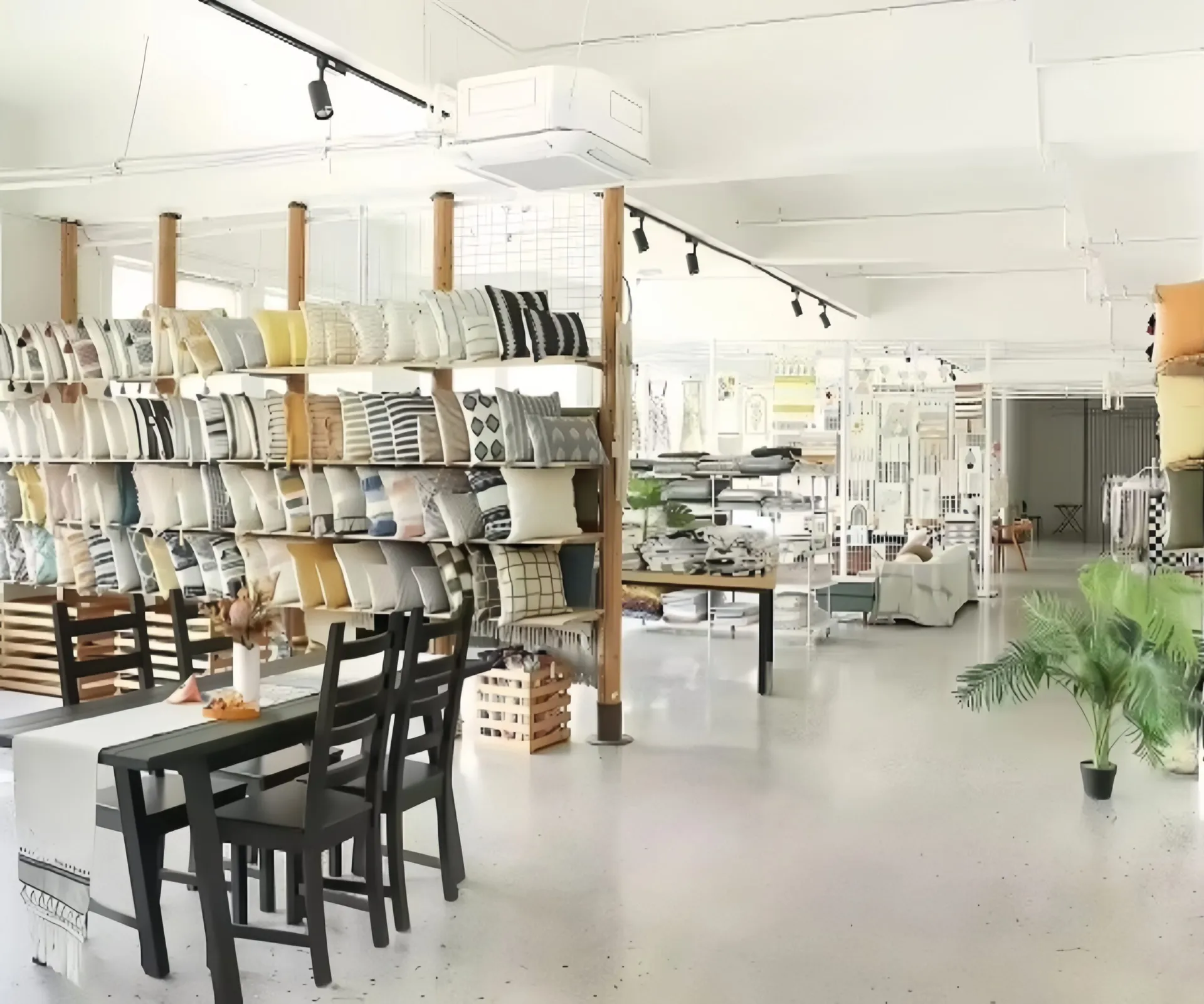 Interior of a showroom with neatly displayed cushions and a black dining table with chairs.