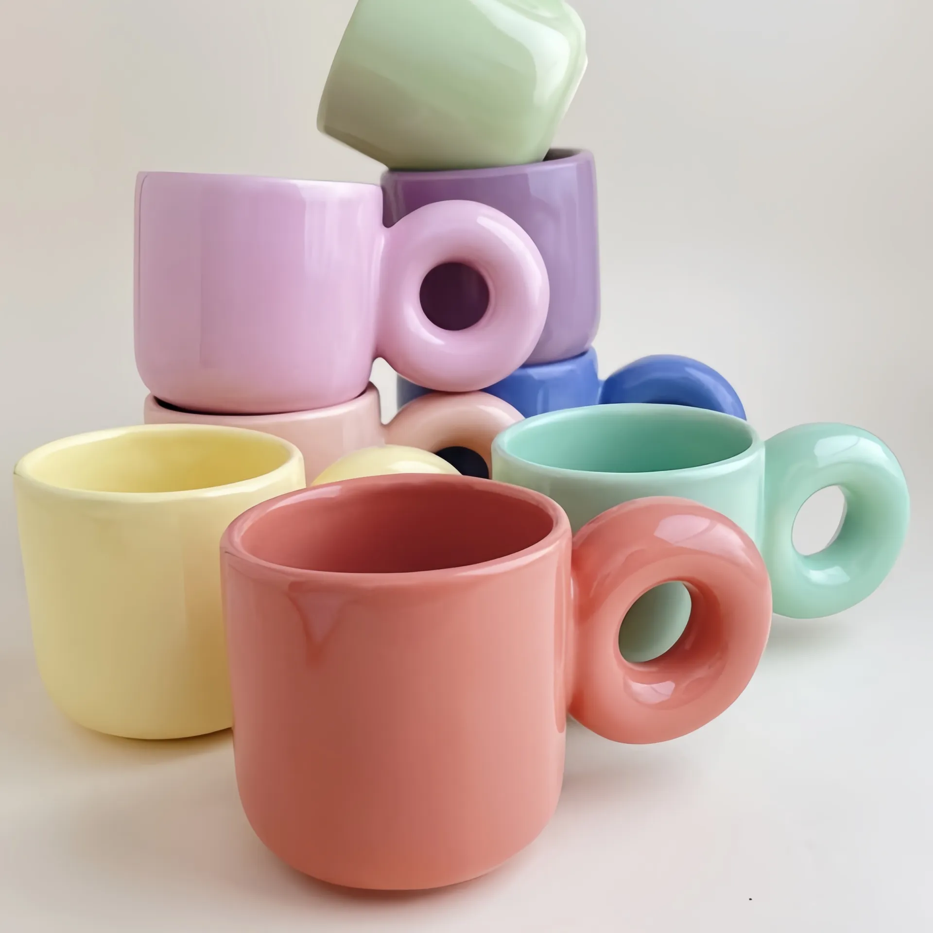 A stack of colorful mugs with circular handles in pastel colors like pink, green, blue, yellow, and peach.