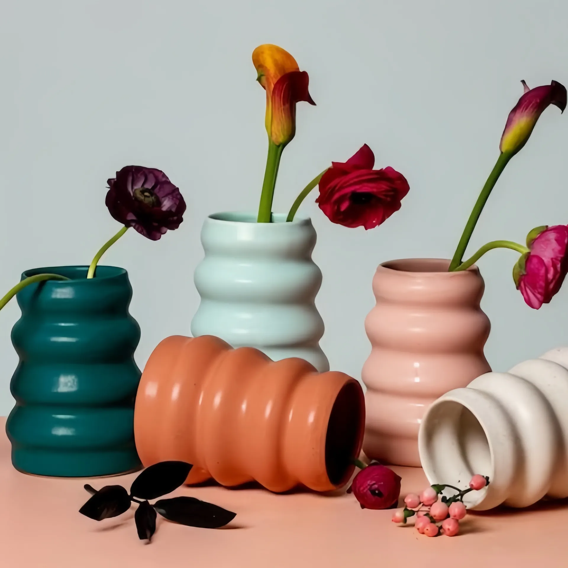 Five sculpted vases in various colors with colorful flowers inserted into them, displayed on a neutral surface.