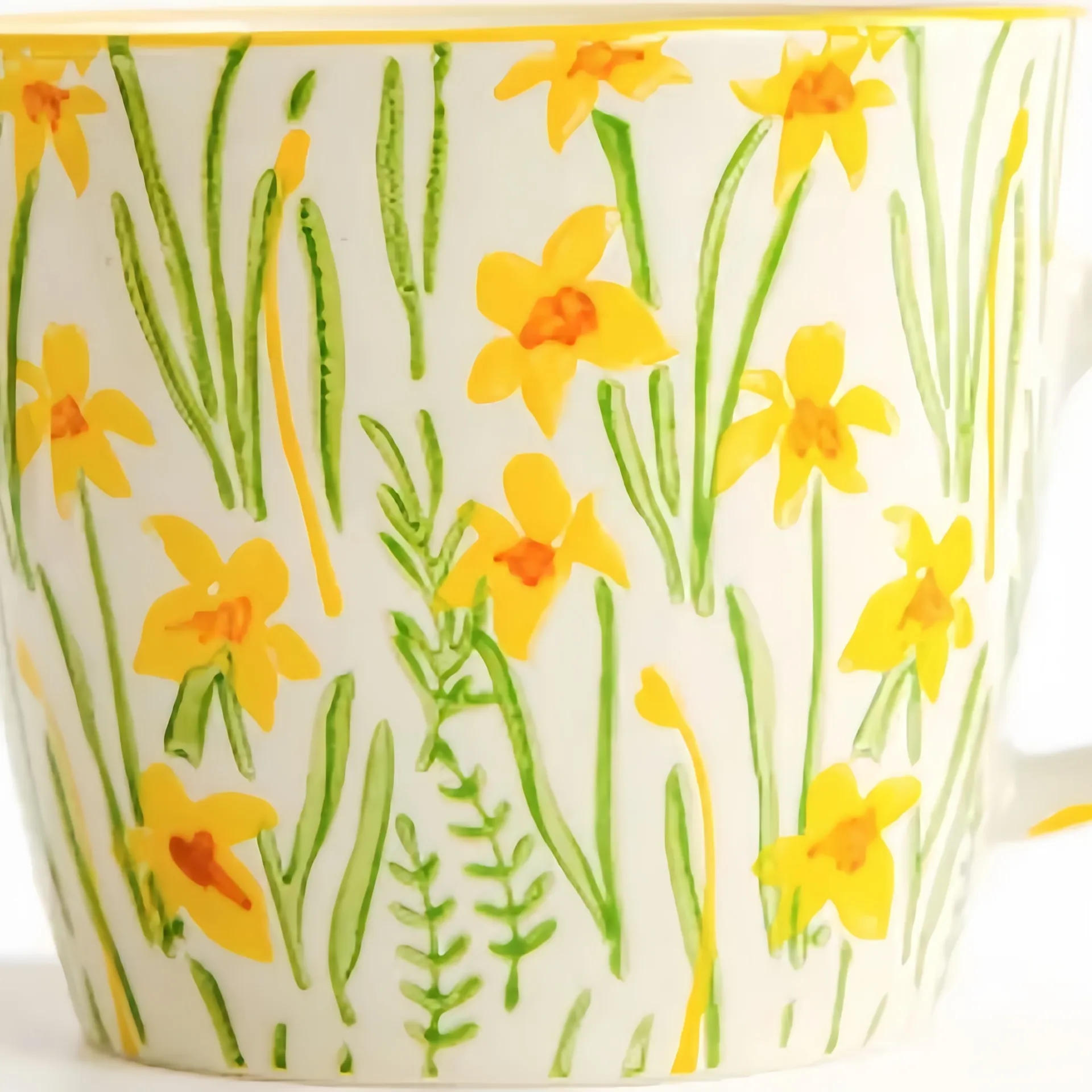 A mug with a pattern of yellow daffodils and green leaves on a white background.