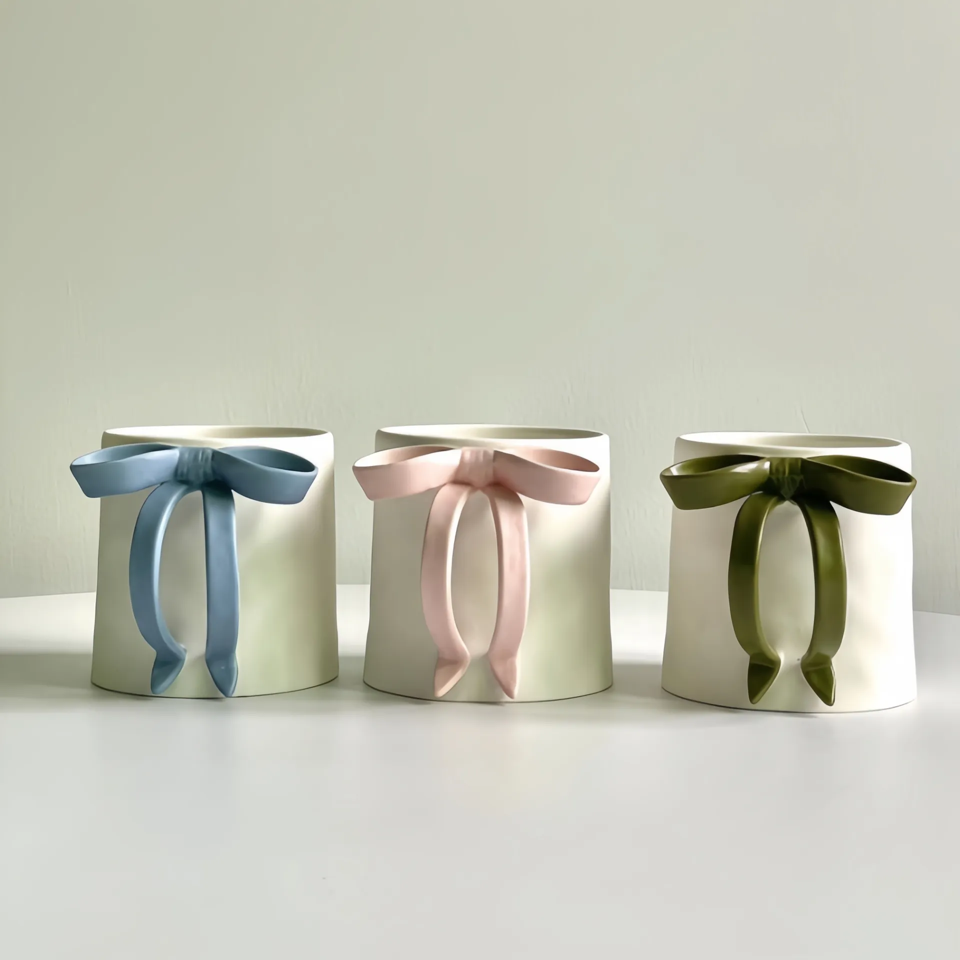 Three white gift boxes with blue, pink, and green bows on a white surface.