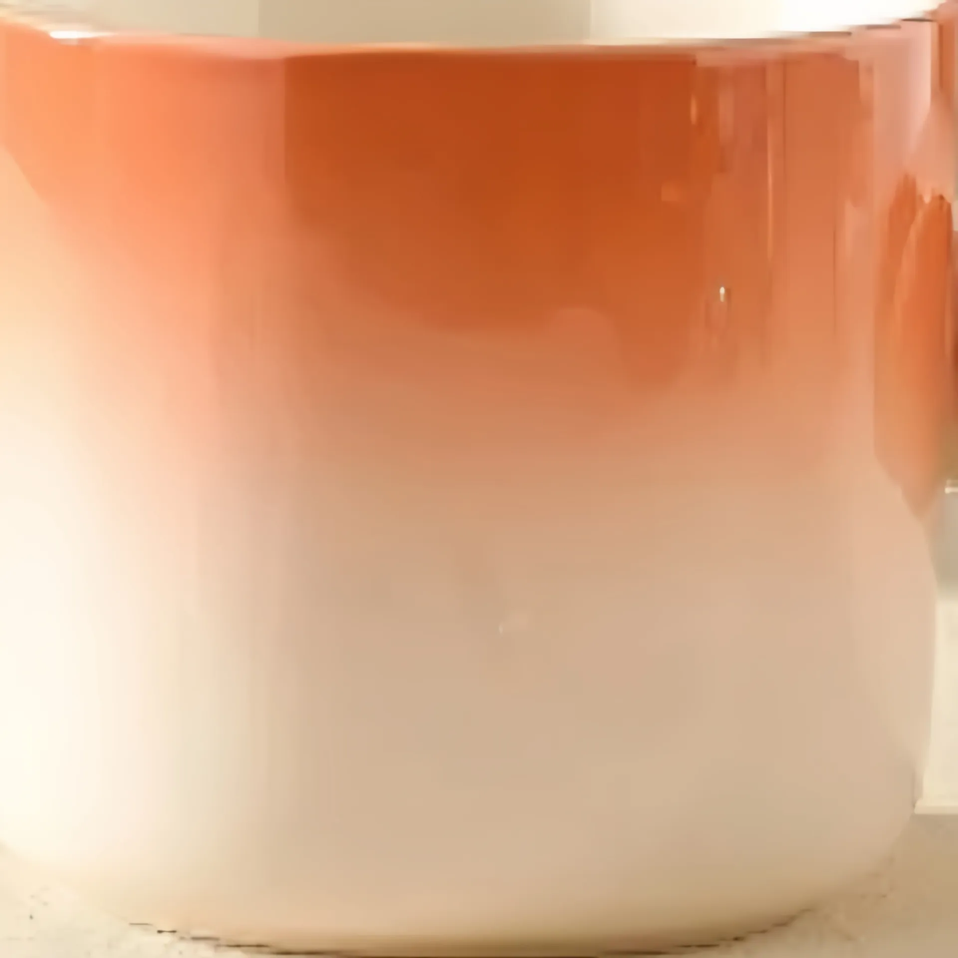 A mug with a gradient from orange to white, placed on a surface.