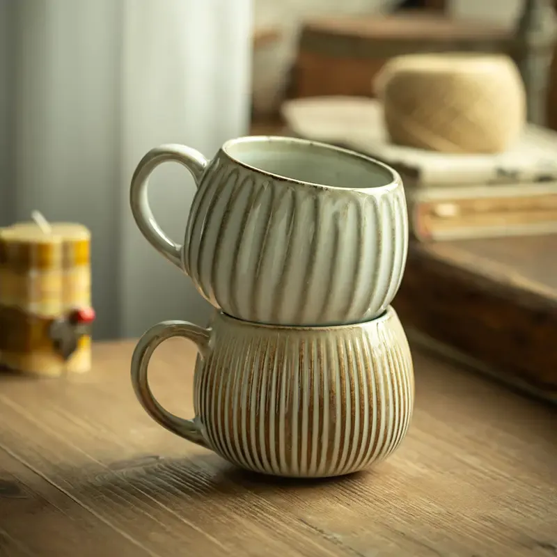 Two ribbed ceramic mugs stacked on a wooden table with a cozy background.