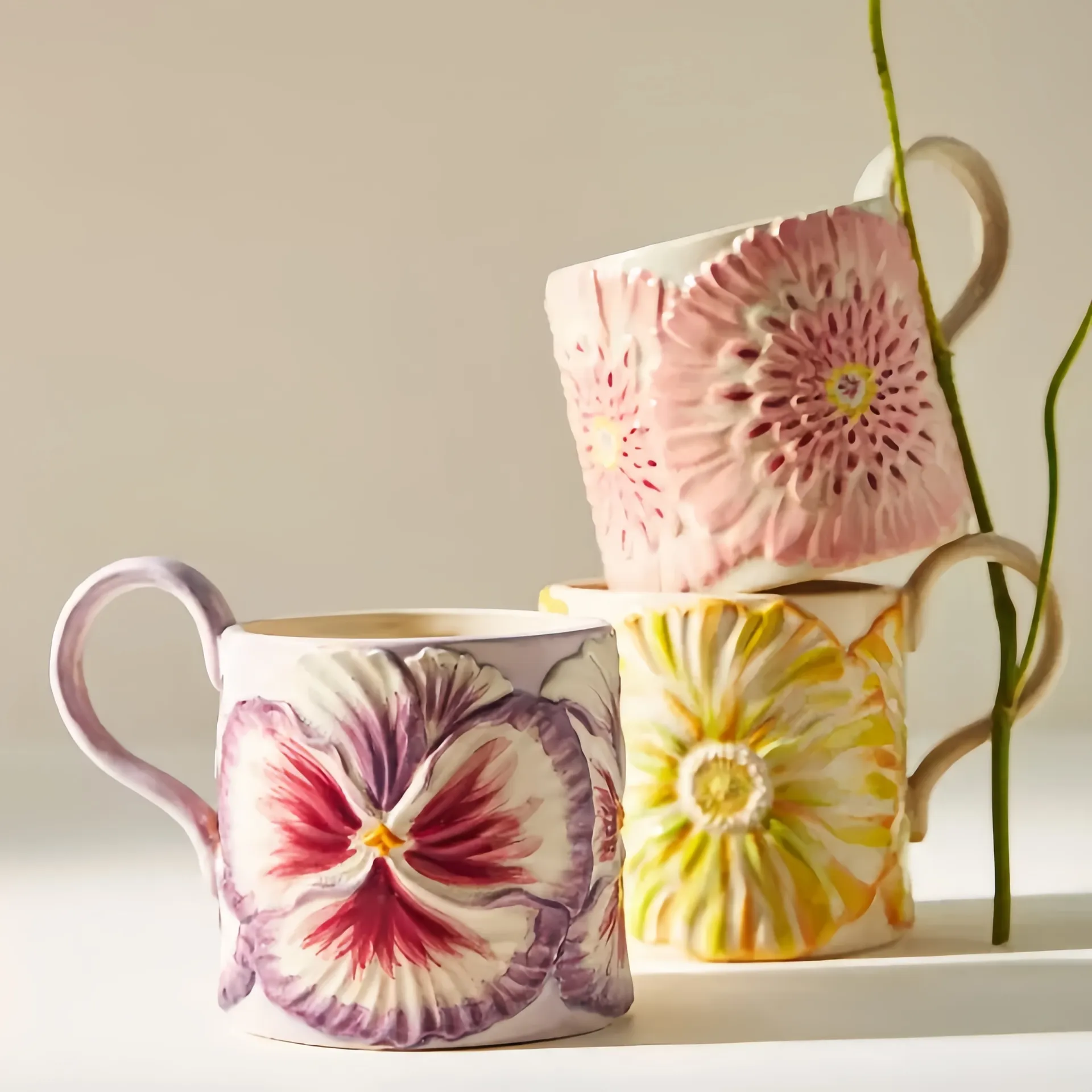 Three ceramic mugs with textured floral designs in pink, purple, and yellow stacked together.