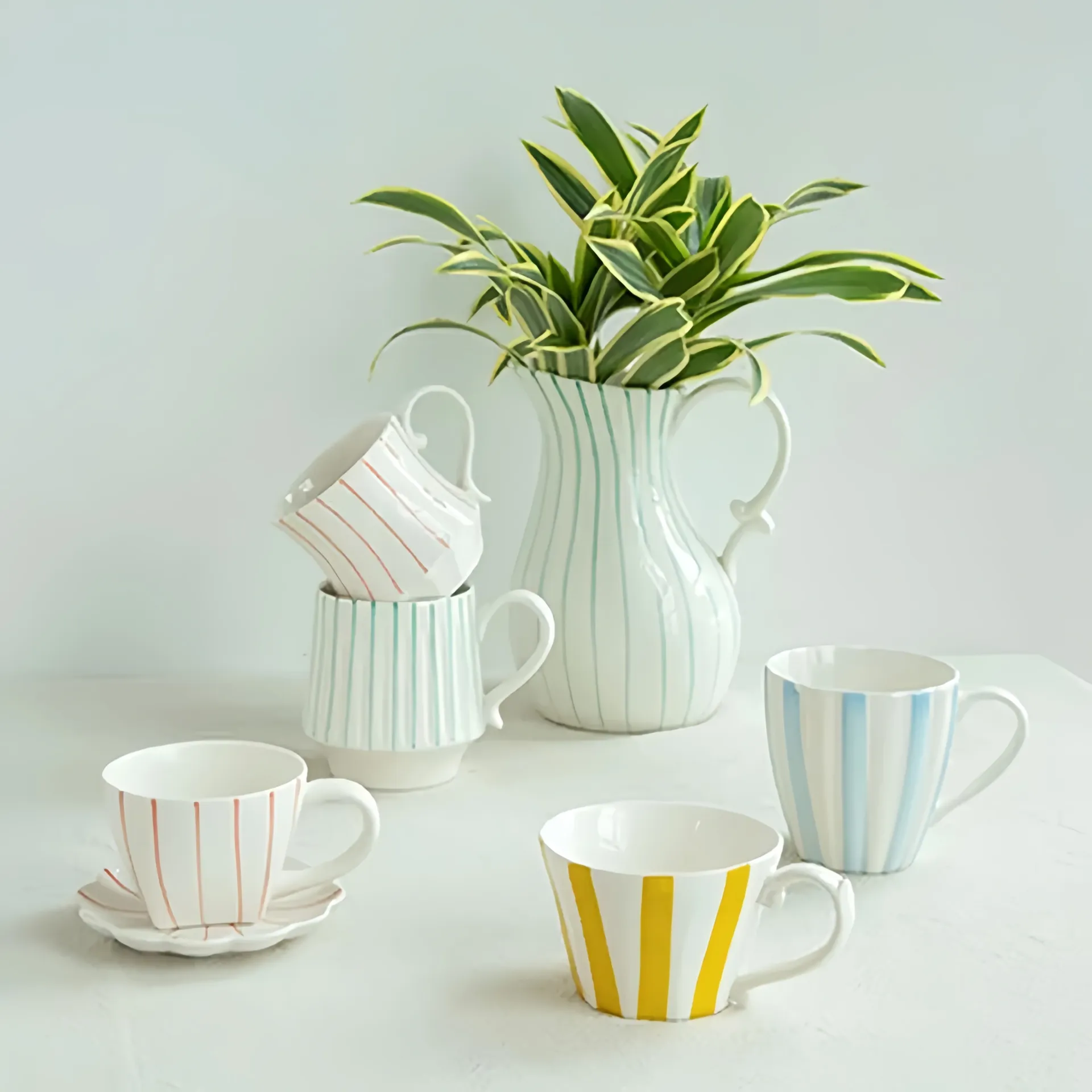 A collection of striped ceramic cups and a pitcher with a plant.